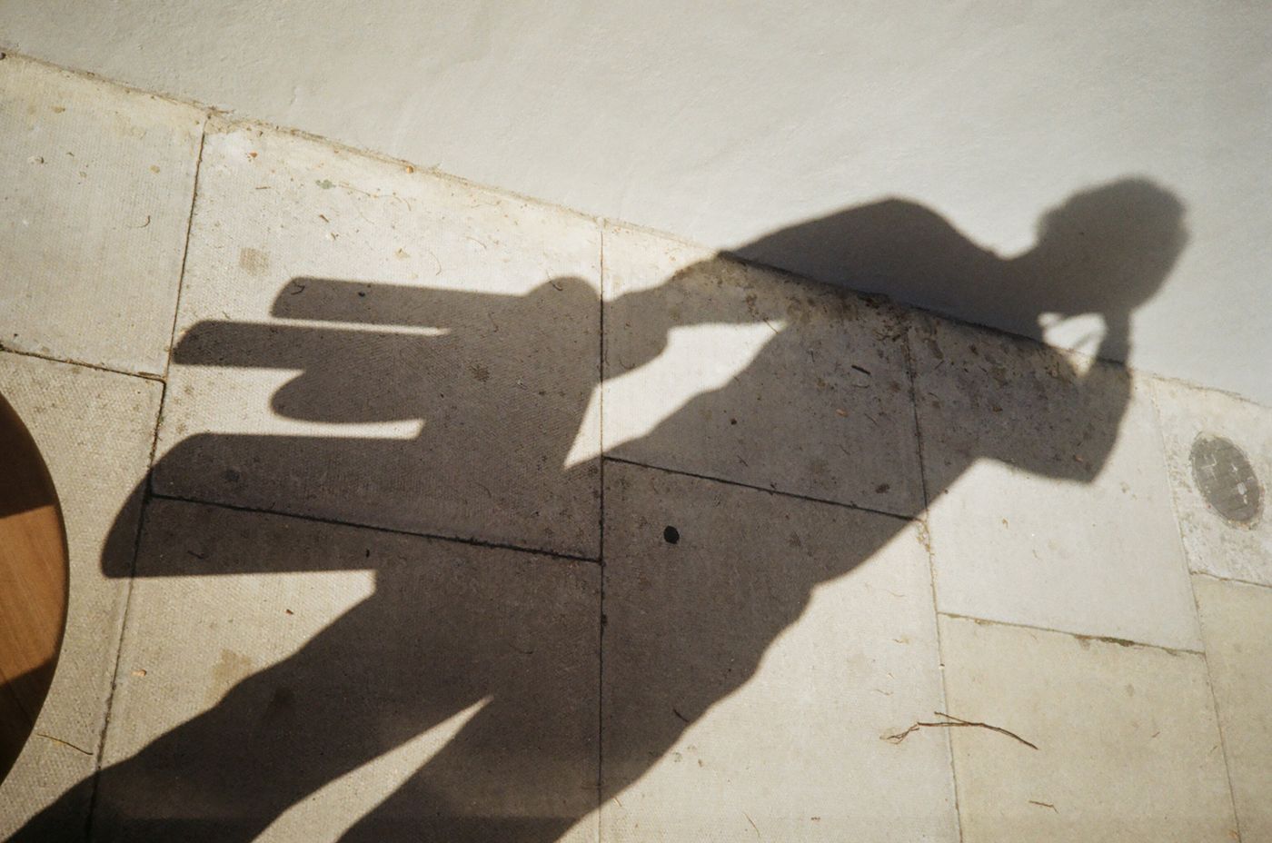 Shadow of a figure holding the stool, cast on the pavement