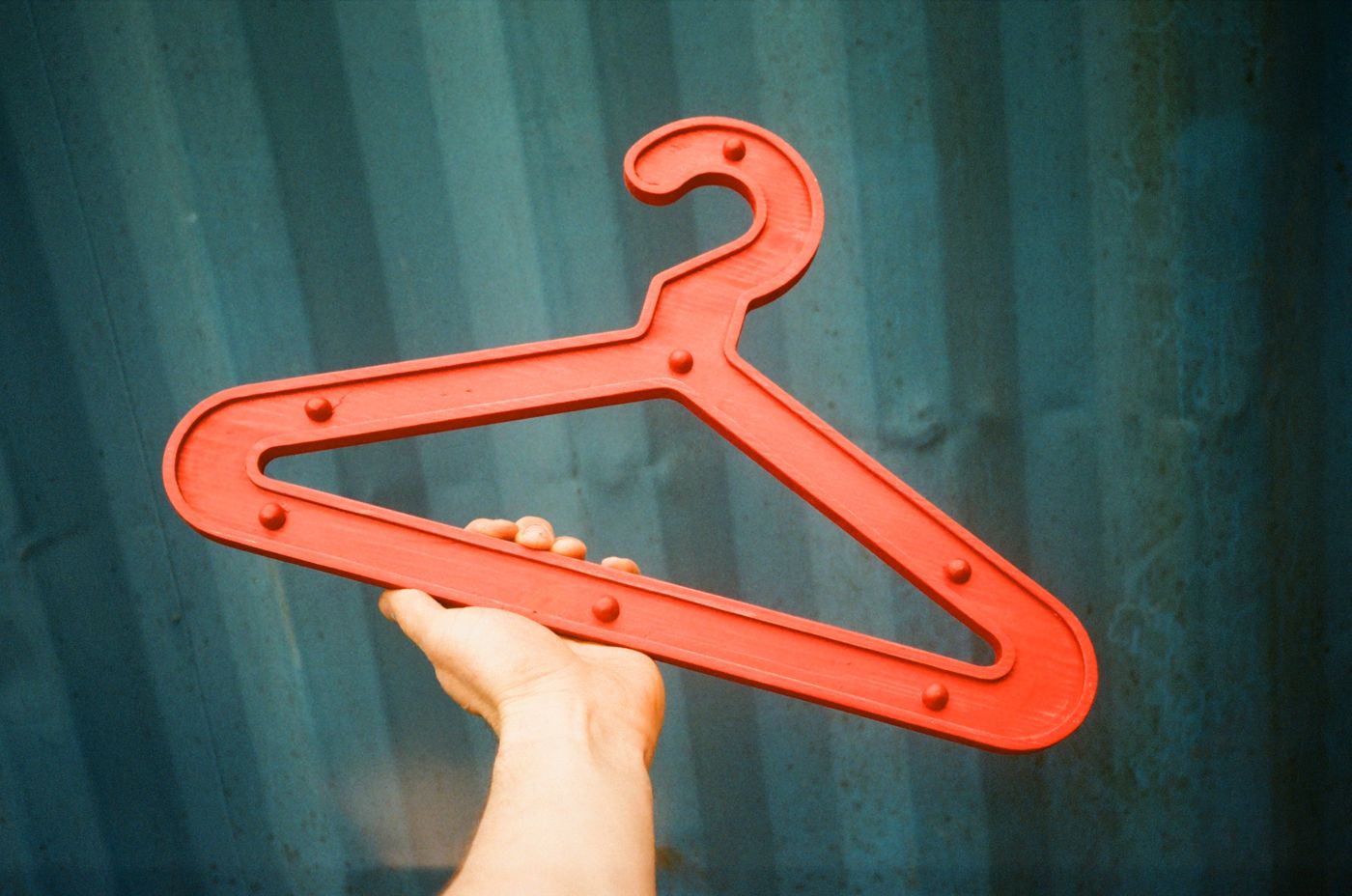 Red Girder Hanger held up against a teal shipping container