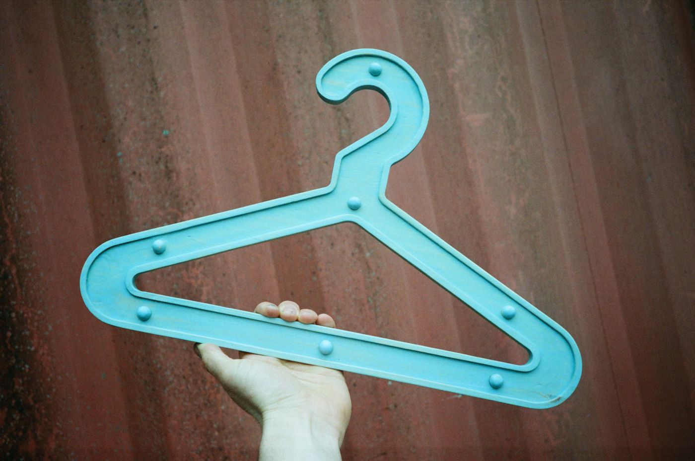 Turquoise Girder Hanger held up against a red shipping container