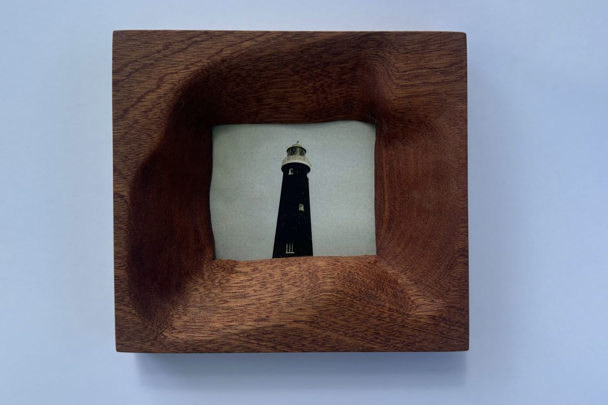 Mahogany frame with a twisting carved opening, holding a photo of a black lighthouse