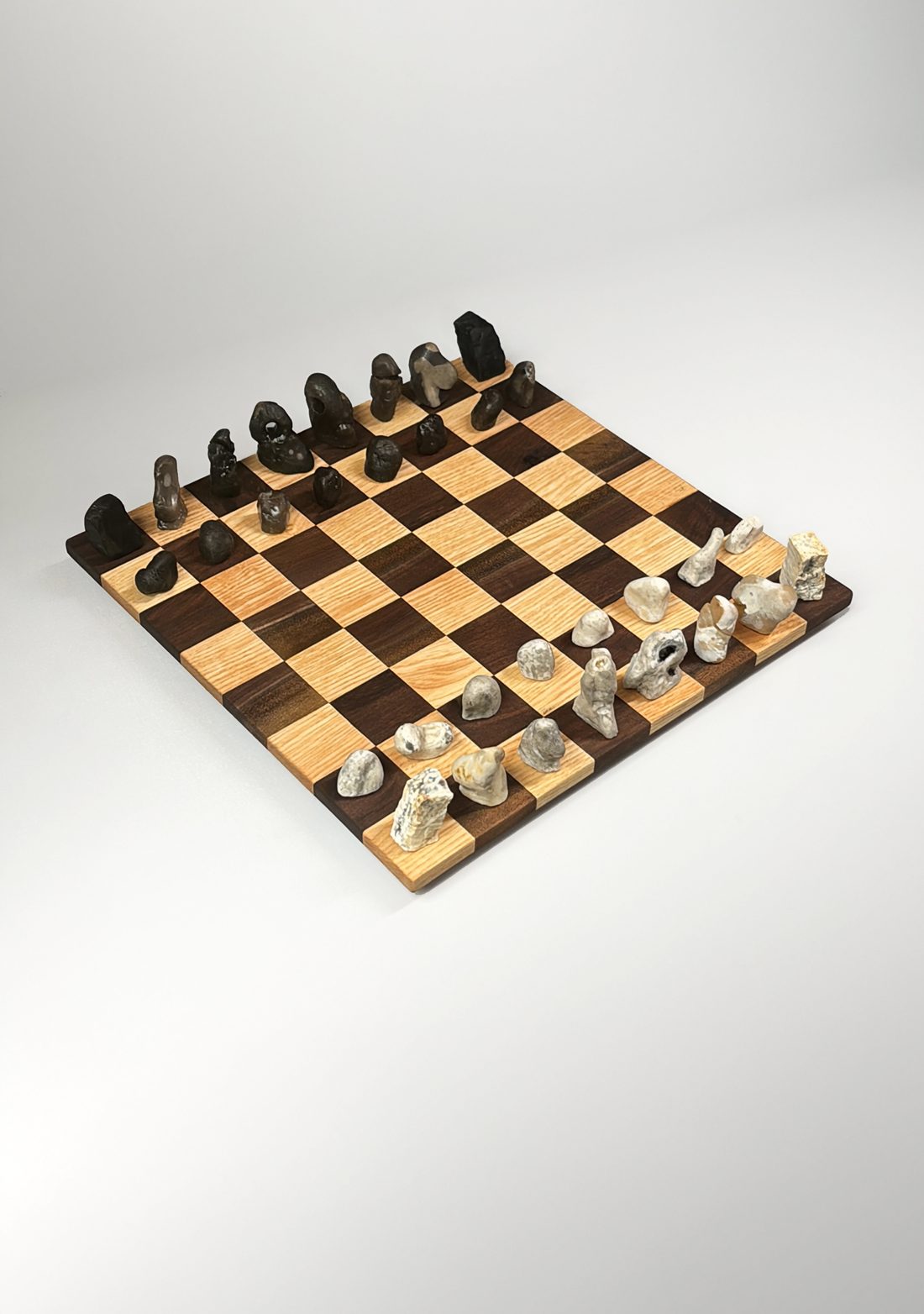 Chess set of found and carved stones, dark against pale, on an oak and walnut chequered board